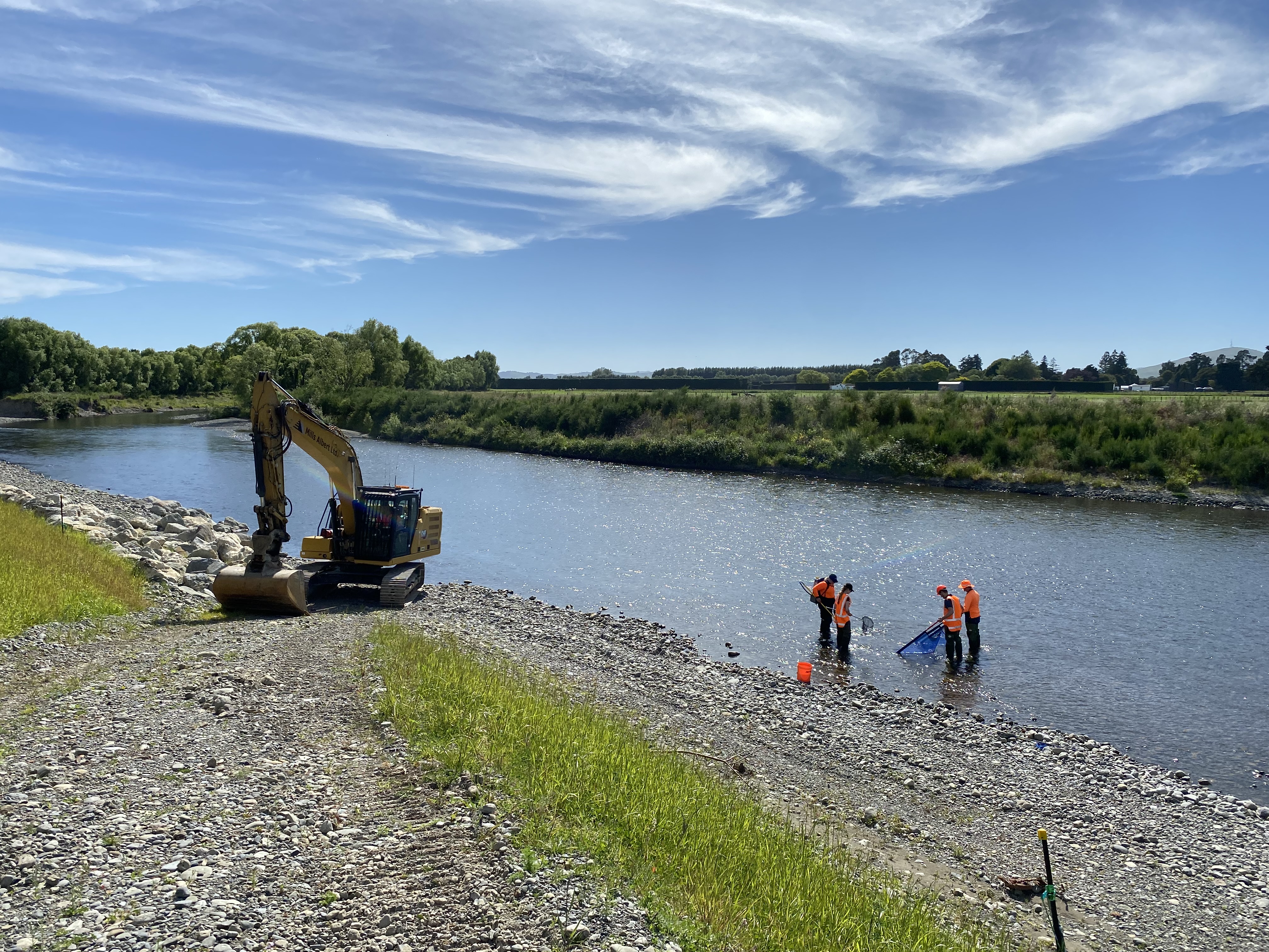 A digger and four people in high-vis vests work at the bank of a river