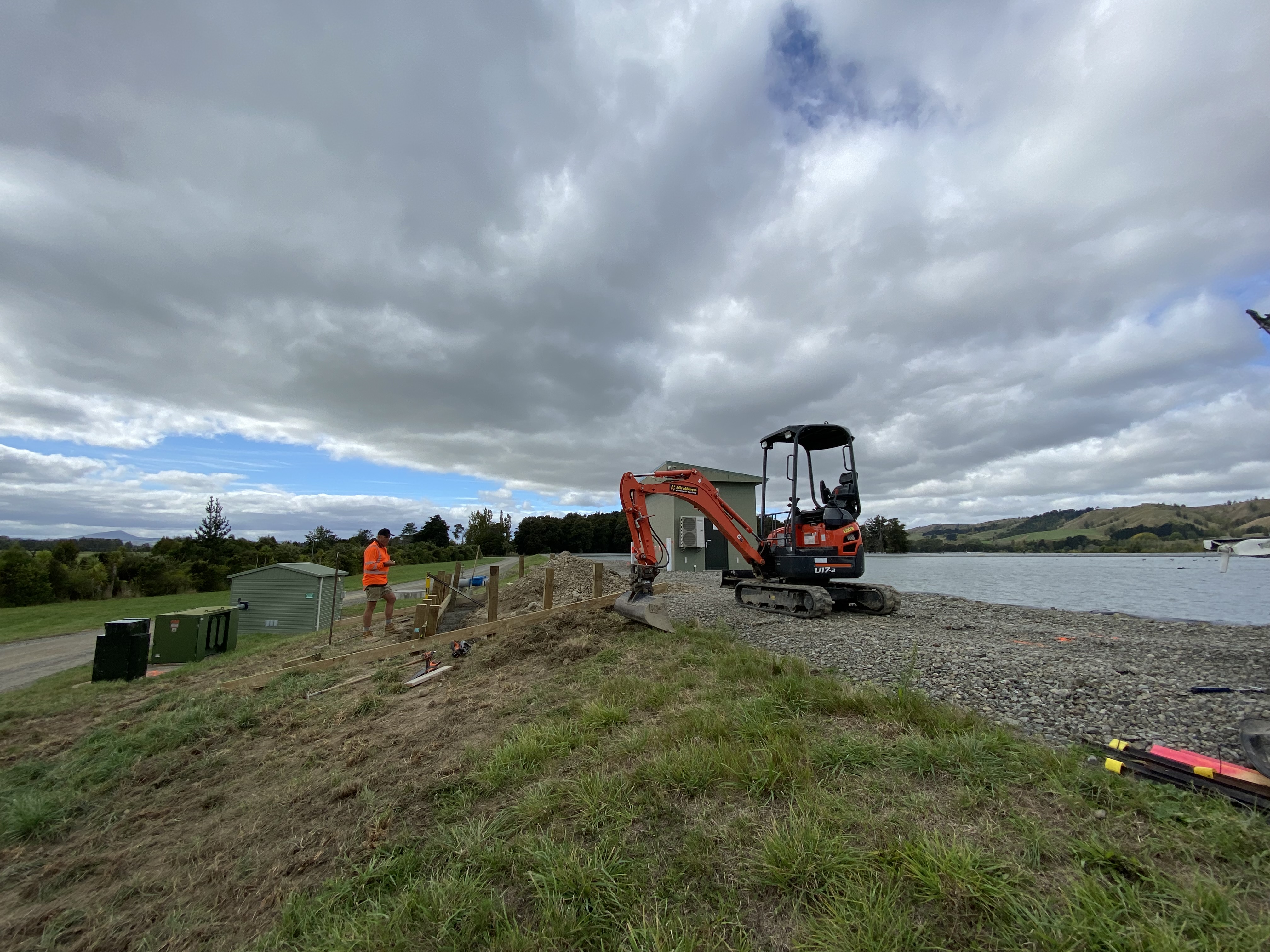 A digger and a person in a high-vis vest on the bank of the Ruamāhanga River