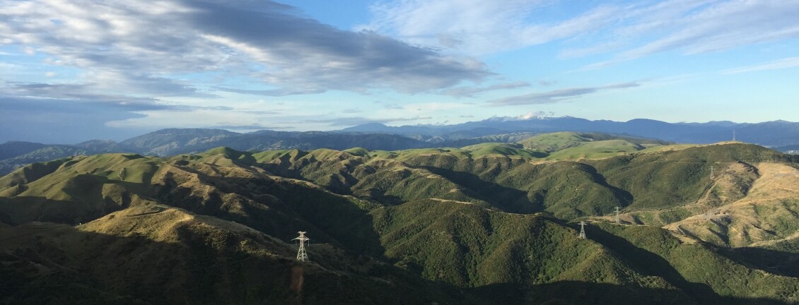 The view from the Belmont Trig on a sunny day; craggy green hills and a bright blue sky with thin clouds