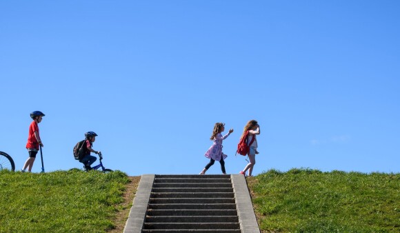 A group of people travelling along the ridge of a hill - an adult on a bike, a child scooting, a child on a bike, two more children walking, and a dog
