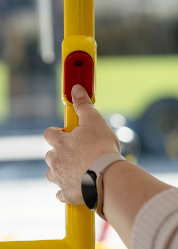 A hand pressing the stop button on a bus